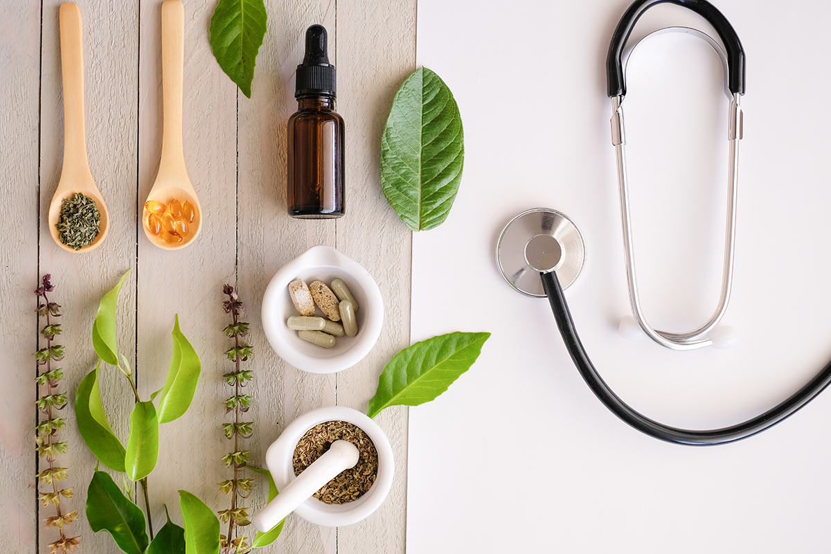 An image with traditional herbs and healing botanicals sitting aside a stethoscope, comparing traditional and integrative healing therapies.